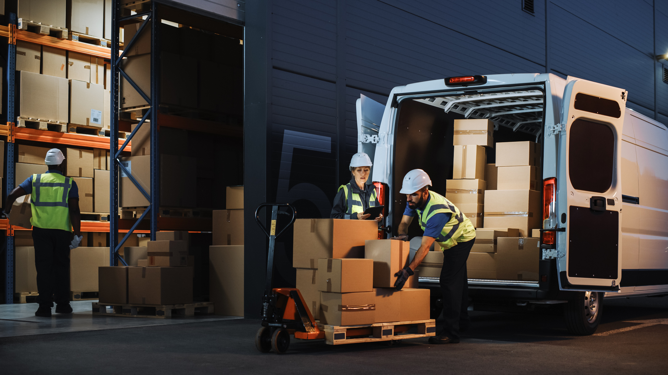 storage facility with cardboard boxes and men in high vis jackets and hard hats moving the boxes from a van